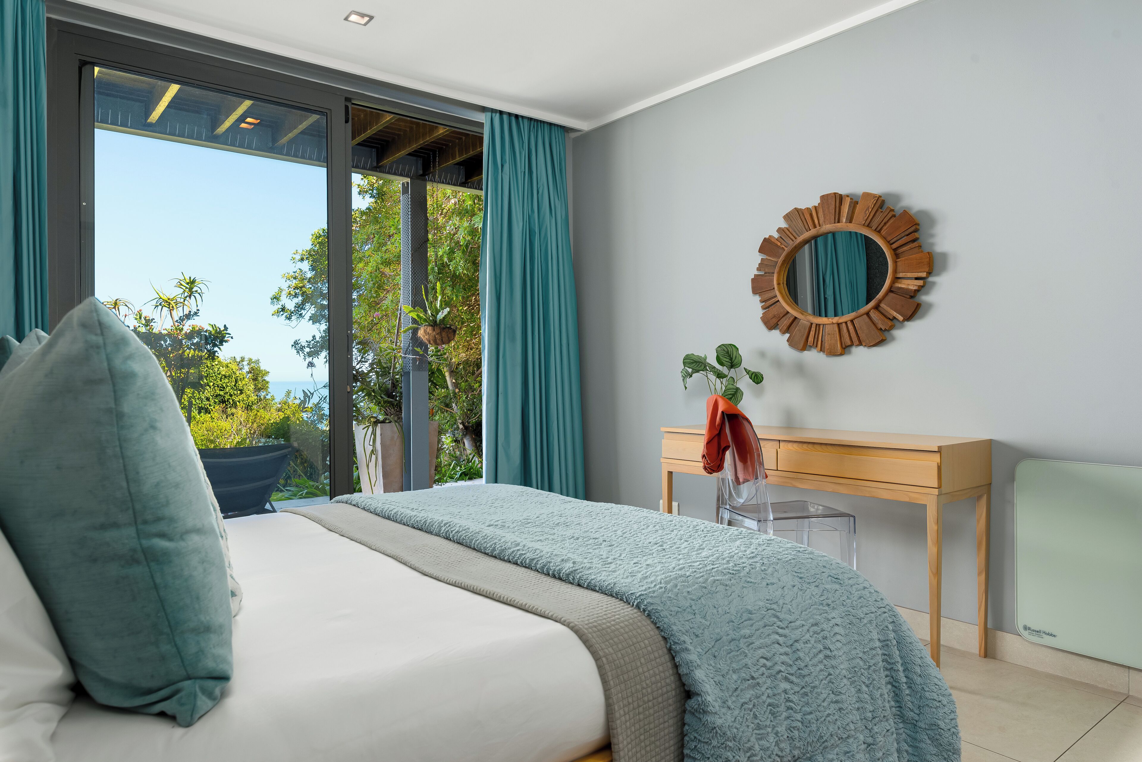 Un dormitorio con una cama grande, un escritorio de madera, un espejo y vistas a zonas verdes.