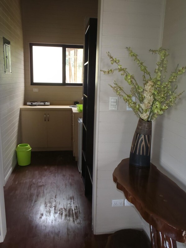 Una cocina compacta con armarios de madera, una ventana y un florero con flores sobre un estante de madera.