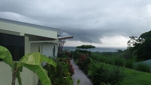 A pathway leading to a building with a covered porch, surrounded by lush greenery and a cloudy sky. - Eden Tica Lodge (Bahía Ballena)