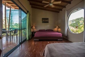 A bedroom with a large bed, a ceiling fan, and a view through a window.
