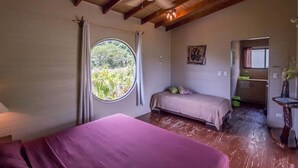 A room with a bed, a smaller bed, a ceiling fan, a window with curtains, and a door leading to another room. - Eden Tica Lodge (Bahía Ballena)