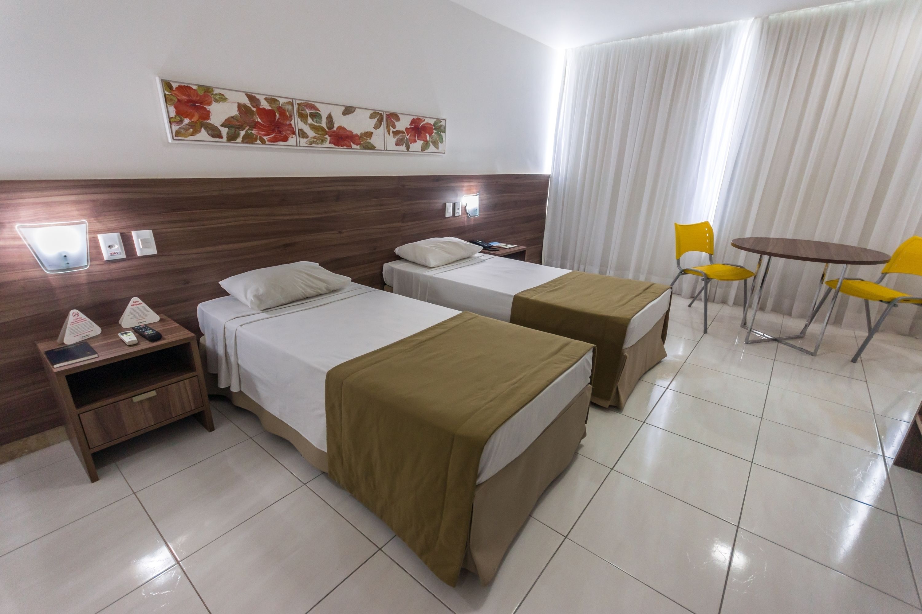 Une chambre d’hôtel avec deux lits, une petite table avec des chaises, une table de chevet et un tableau au mur.