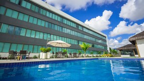 A modern hotel with a swimming pool, outdoor seating, and a large building facade. - Cambuci Hotel (Camaçari)