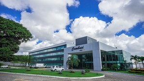 A modern hotel building with a glass facade, a well-maintained lawn, and a parking area with several cars. - Cambuci Hotel (Camaçari)