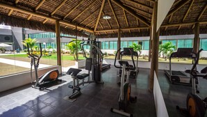 An indoor gym with exercise equipment, large windows, and a thatched roof. - Cambuci Hotel (Camaçari)