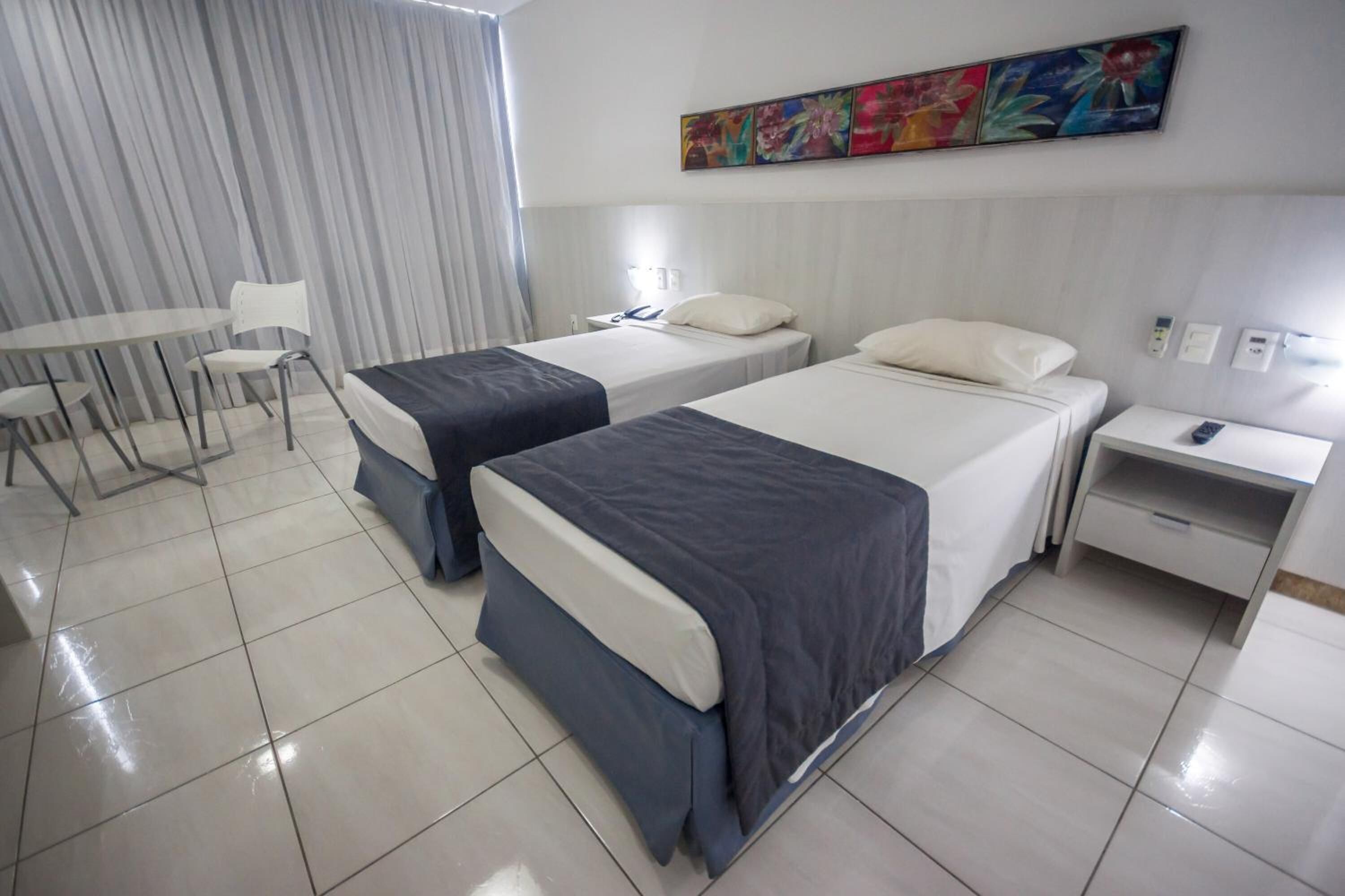 Habitación de hotel con dos camas, una mesita, sillas, un escritorio y un cuadro en la pared.