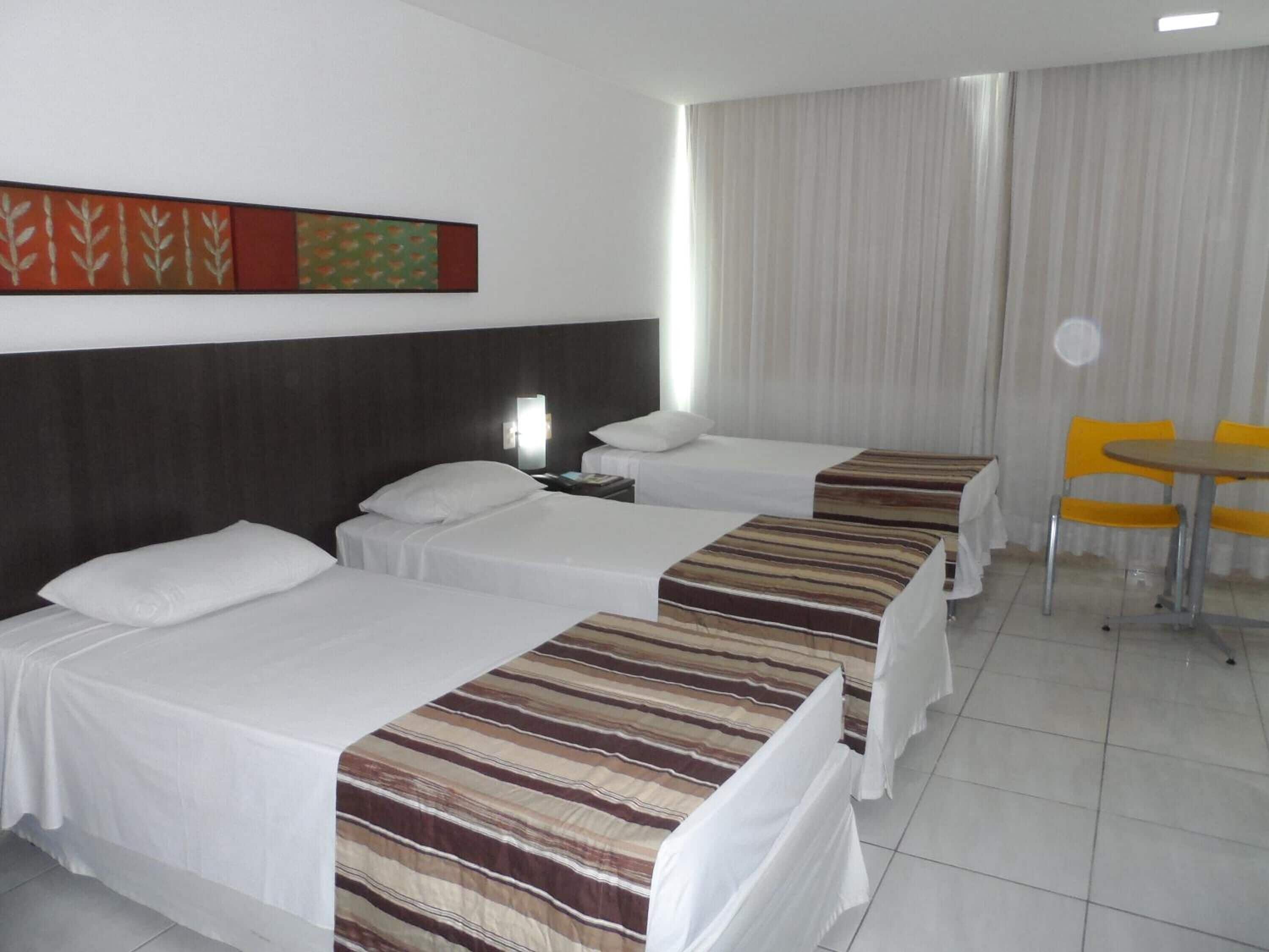 Une chambre d’hôtel avec trois lits, une petite table et une chaise.