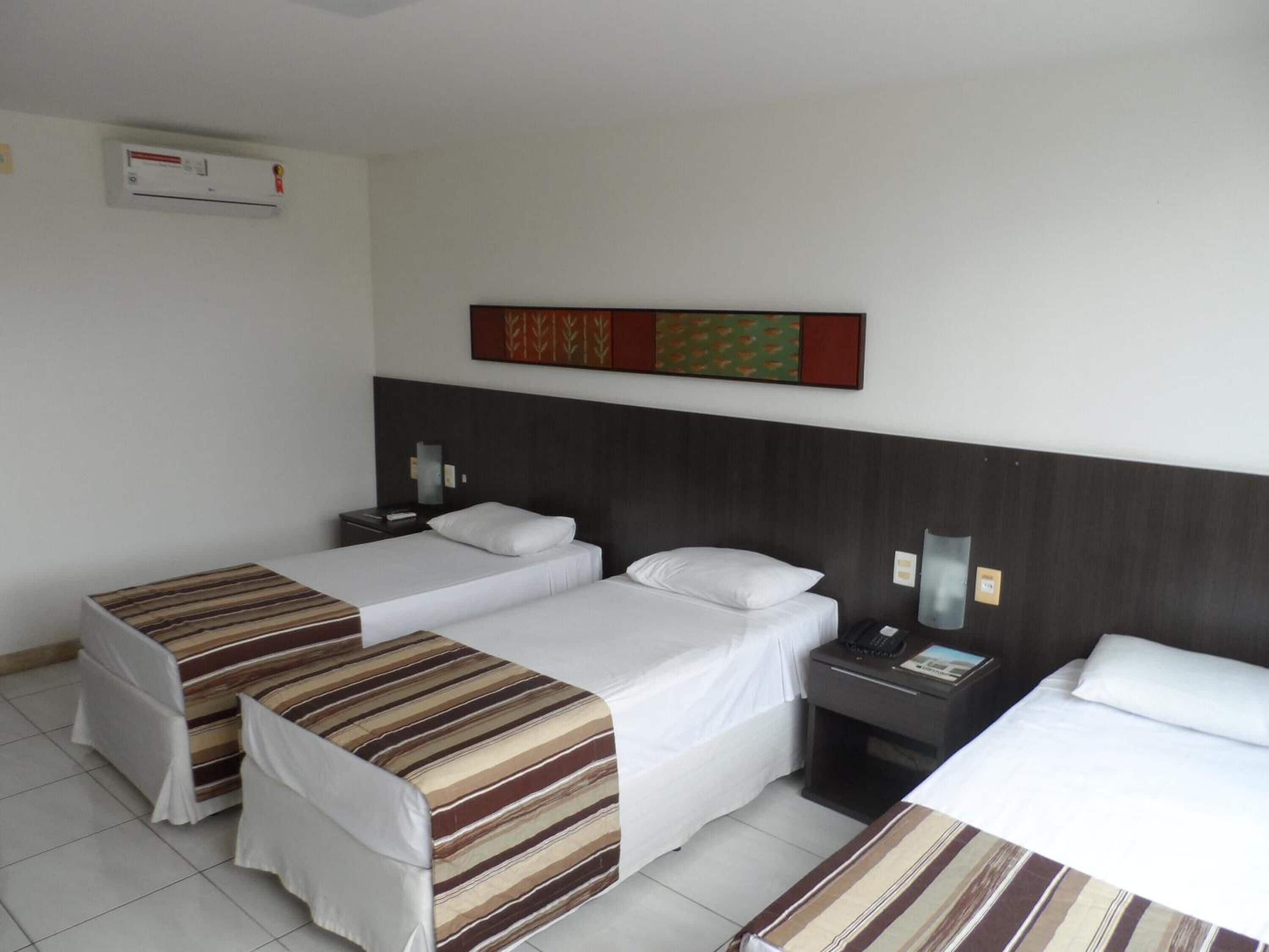 Una habitación de hotel con dos camas individuales, una mesita de noche con lámpara y un aire acondicionado instalado en la pared.