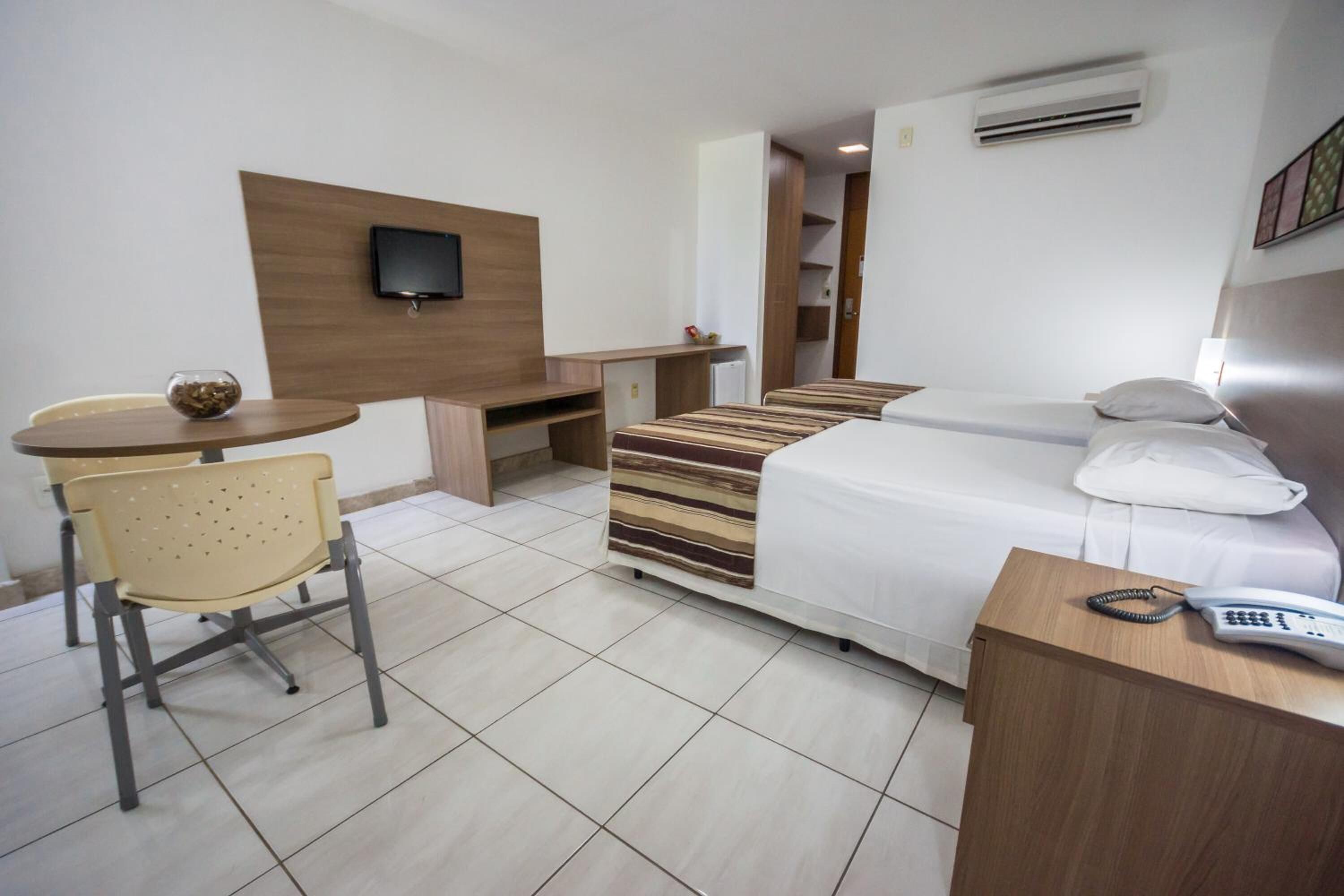 A hotel room with a bed, a desk, a chair, a TV, and a phone.