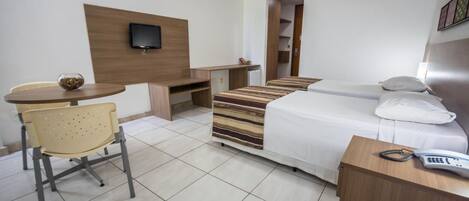 A hotel room with a bed, a desk, a chair, a TV, and a phone.