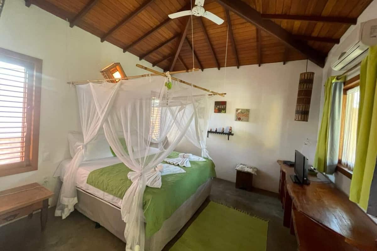 Ein Schlafzimmer mit einem Himmelsbett, einem Schreibtisch mit Computer und einem Fenster mit Vorhängen.