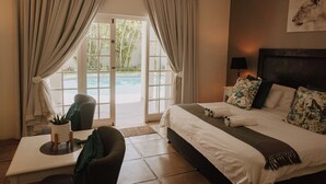 Ein Hotelzimmer mit einem Bett, einem Schreibtisch, einem Sessel, einem kleinen Tisch mit Pflanze und Blick auf einen Pool durch eine Glastür.