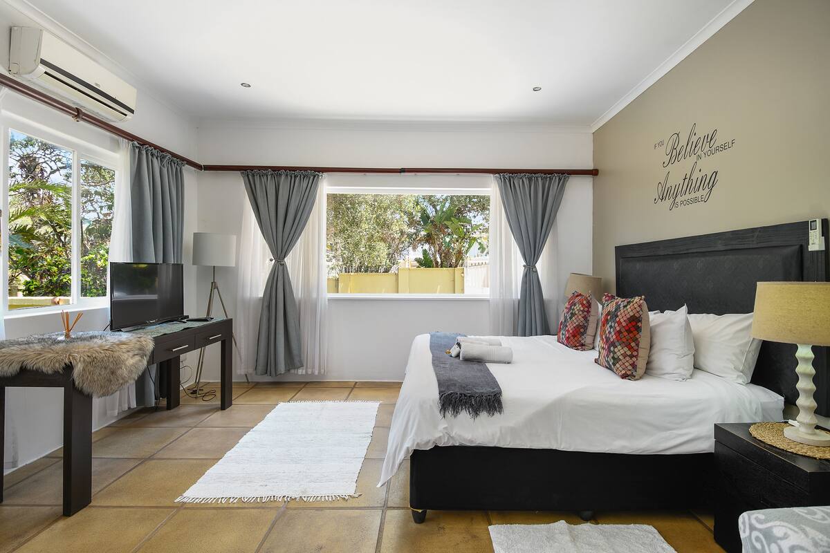 Une chambre à coucher avec un lit, une télévision, un bureau et une fenêtre avec des rideaux.