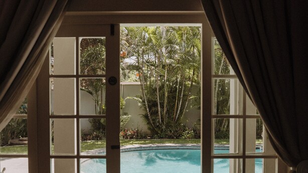 Blick durch eine Glastür auf einen Pool mit einer gefliesten Terrasse.
