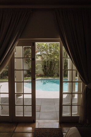 Blick durch eine Glastür auf einen Pool mit einer gefliesten Terrasse.