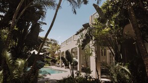 Ein Pool, umgeben von üppiger tropischer Vegetation und einem modernen Gebäude mit Bogenbalkonen.