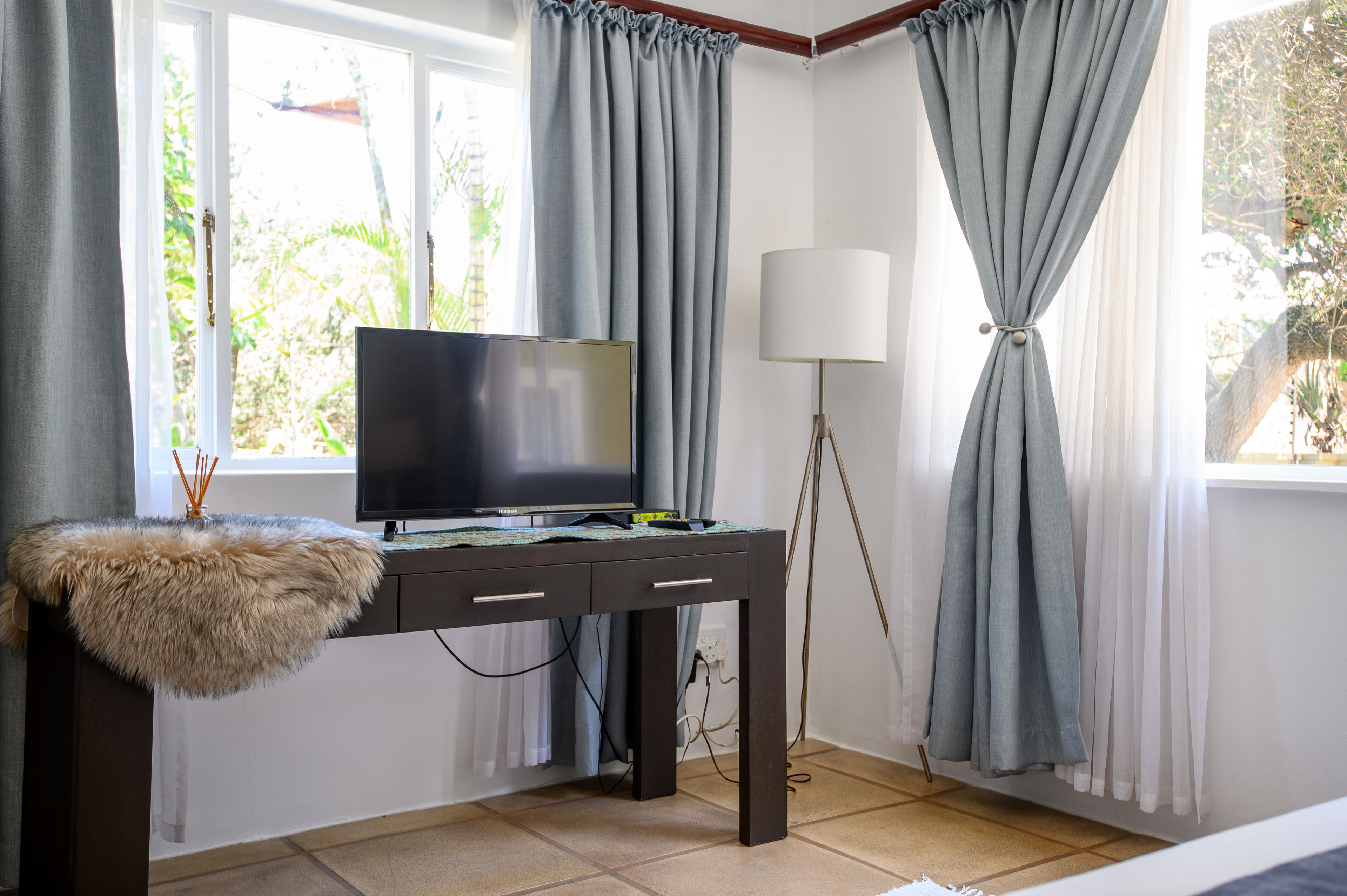 Quarto com escrivaninha, televisão, candeeiro e vista para o verde lá fora.