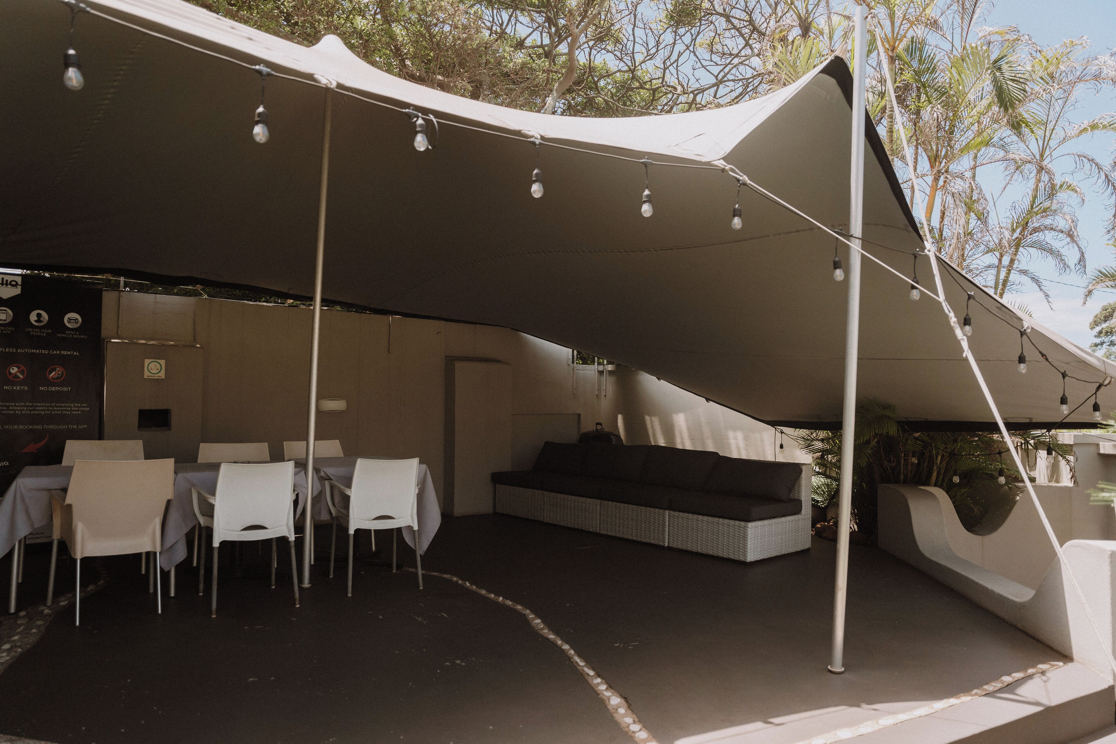 Un espace extérieur aménagé avec des tables et des chaises sous une marquise, un canapé et un luminaire fixé au mur.