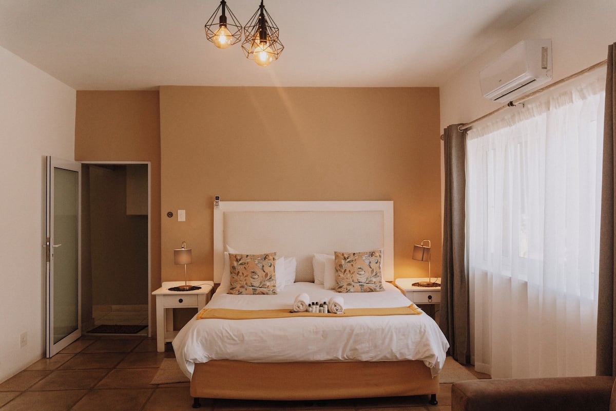 Une chambre d’hôtel avec un grand lit, des tables de chevet, une commode, un banc, une porte et un appareil de climatisation.