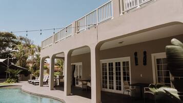 A poolside area with lounge chairs, a covered patio, and a building with large windows and a balcony.