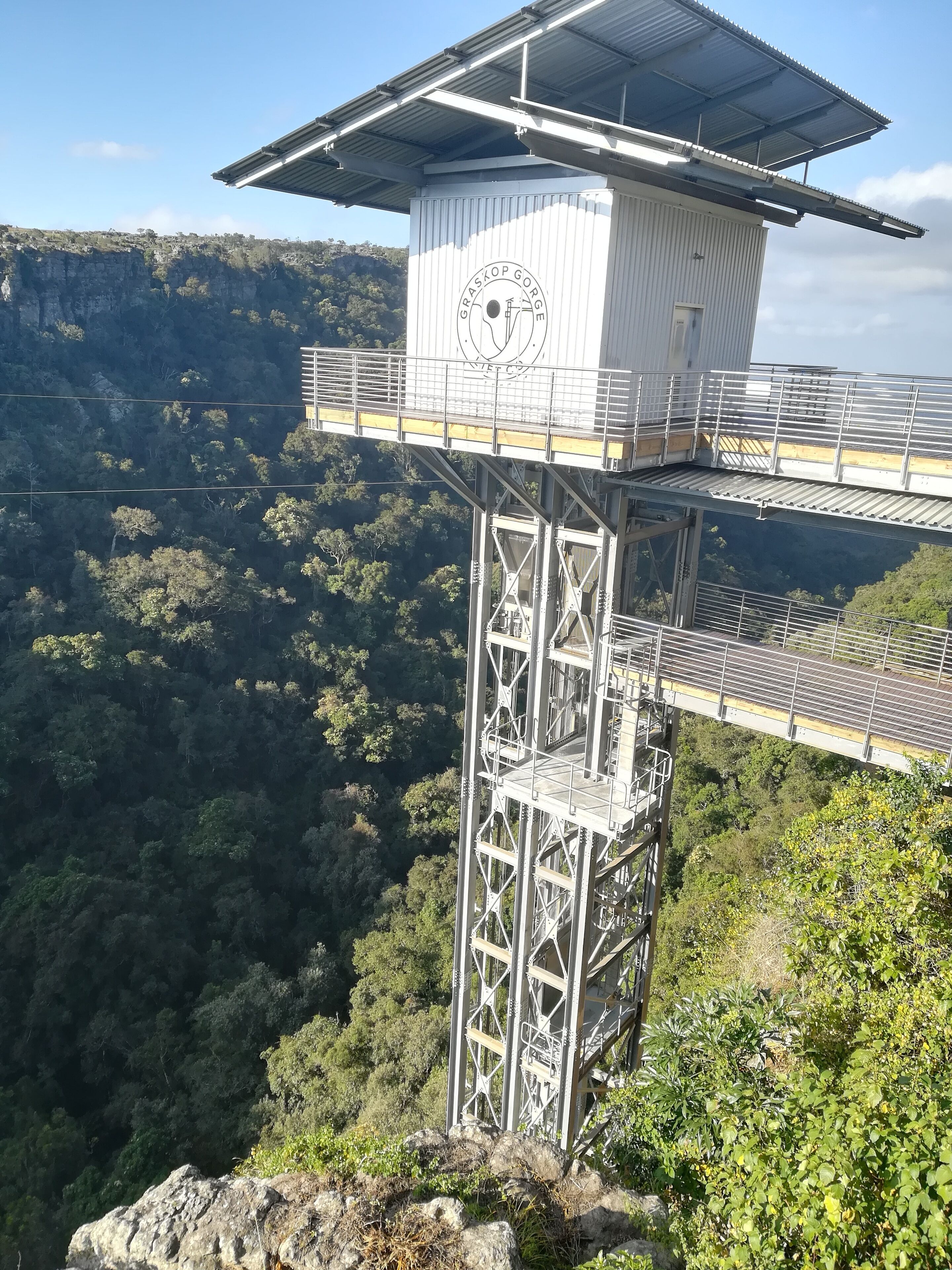 A high observation tower with a metal framework and a flat roof, overlooking a forested valley.