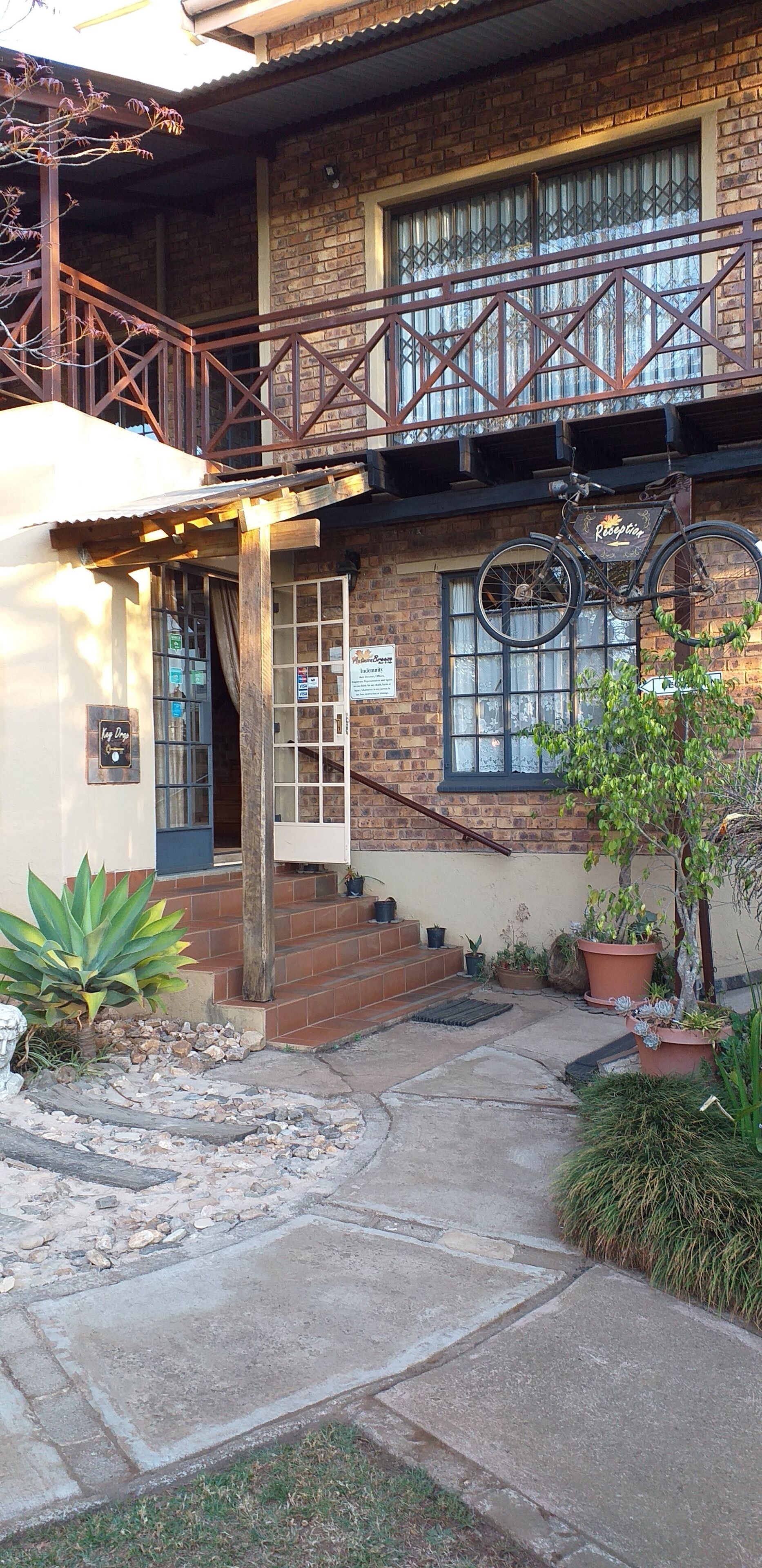 A brick building with a wooden balcony, a bicycle hanging on the wall, and potted plants in the courtyard.