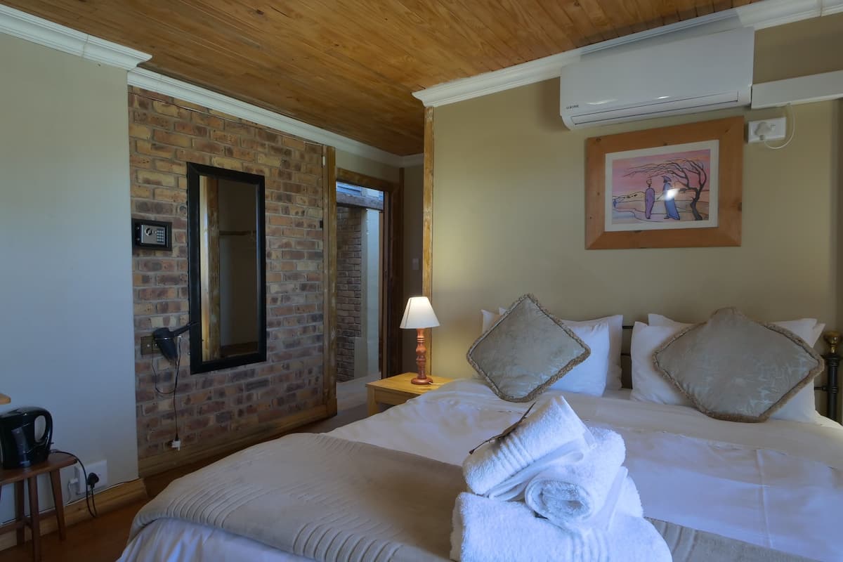 A hotel room with a brick wall, a large bed with white linens, a framed picture on the wall, and an air conditioning unit.