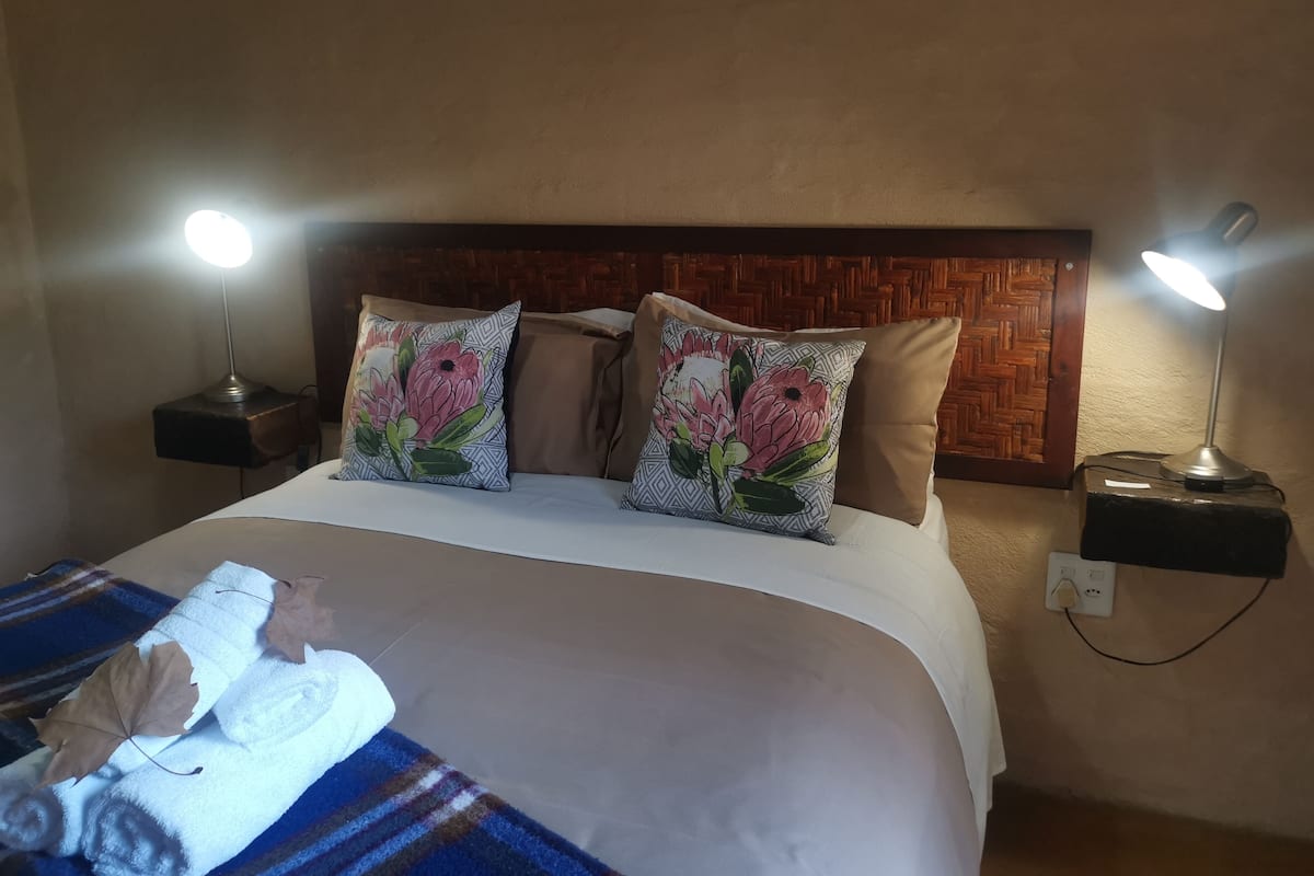 A hotel room with a bed, two bedside lamps, a wooden headboard, and a blanket with a leaf pattern.