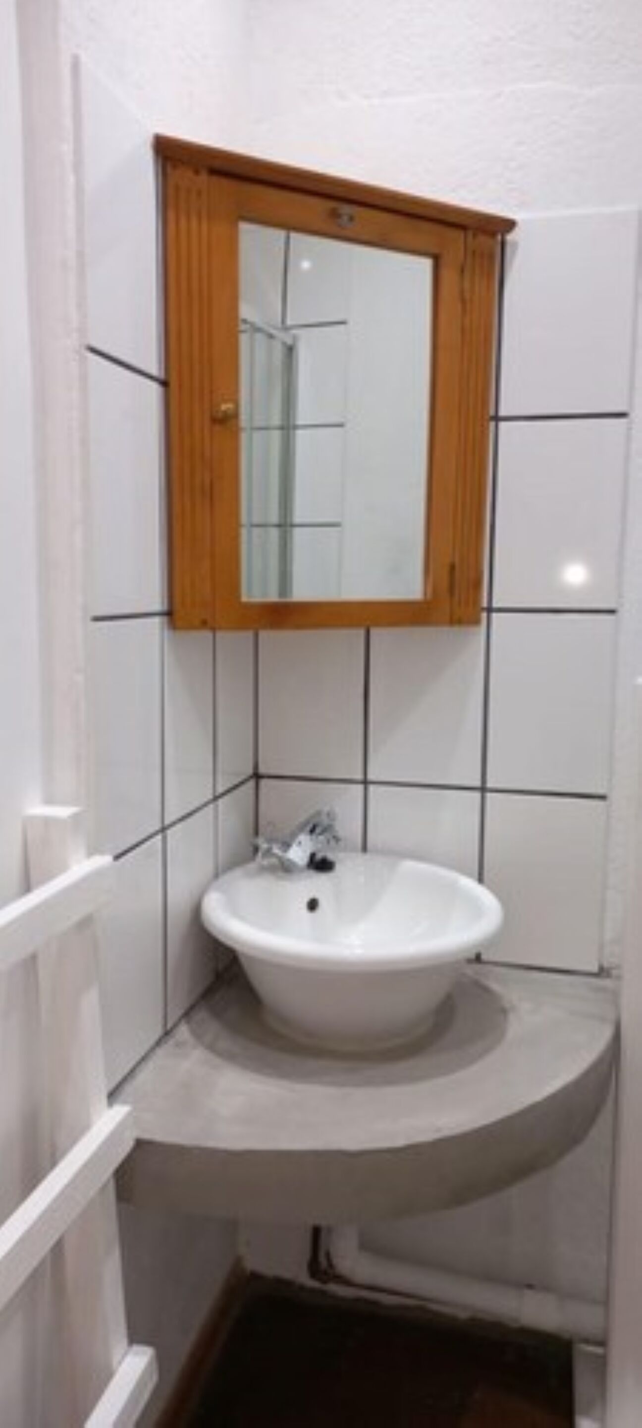 A bathroom with a white sink, a wooden medicine cabinet, and white tiled walls.