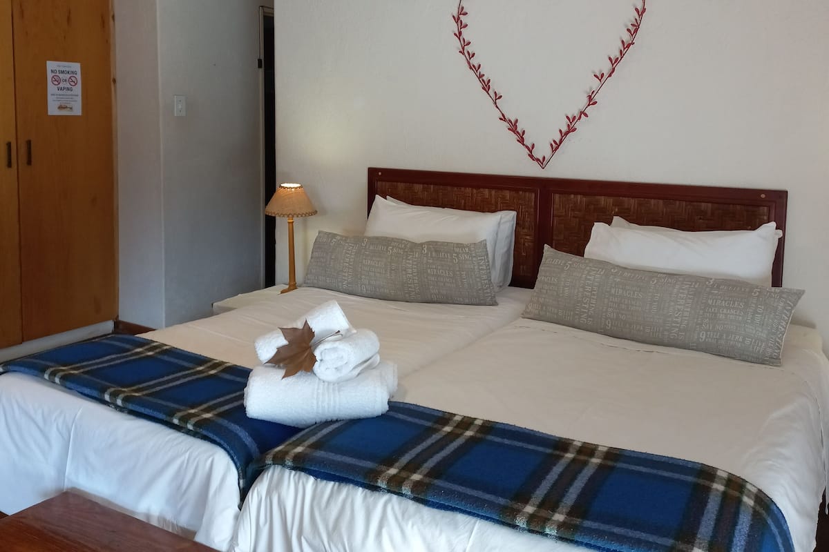 A hotel room with a bed, a heart-shaped decoration on the wall, a sign prohibiting smoking, and a lamp.