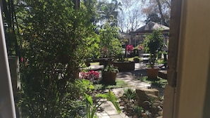 Un patio jardín con plantas en macetas, suelo de baldosas y vista de un edificio al fondo.