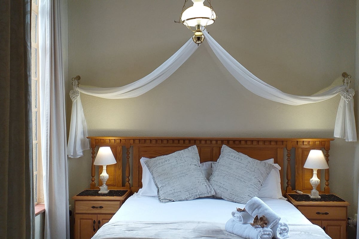 A bedroom with a canopy bed, two bedside lamps, and a nightstand with a lamp.