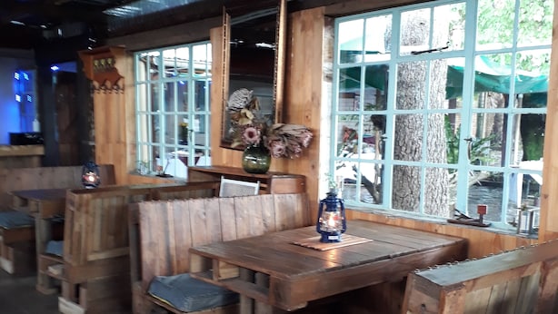Un interior rústico de madera con bancos y mesas, ventanas amplias con vistas a la vegetación y un techo de estilo rústico.
