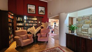 A library with bookshelves, two armchairs, a reception desk, and a stone wall. - Ash River Lodge B&B (Clarens)