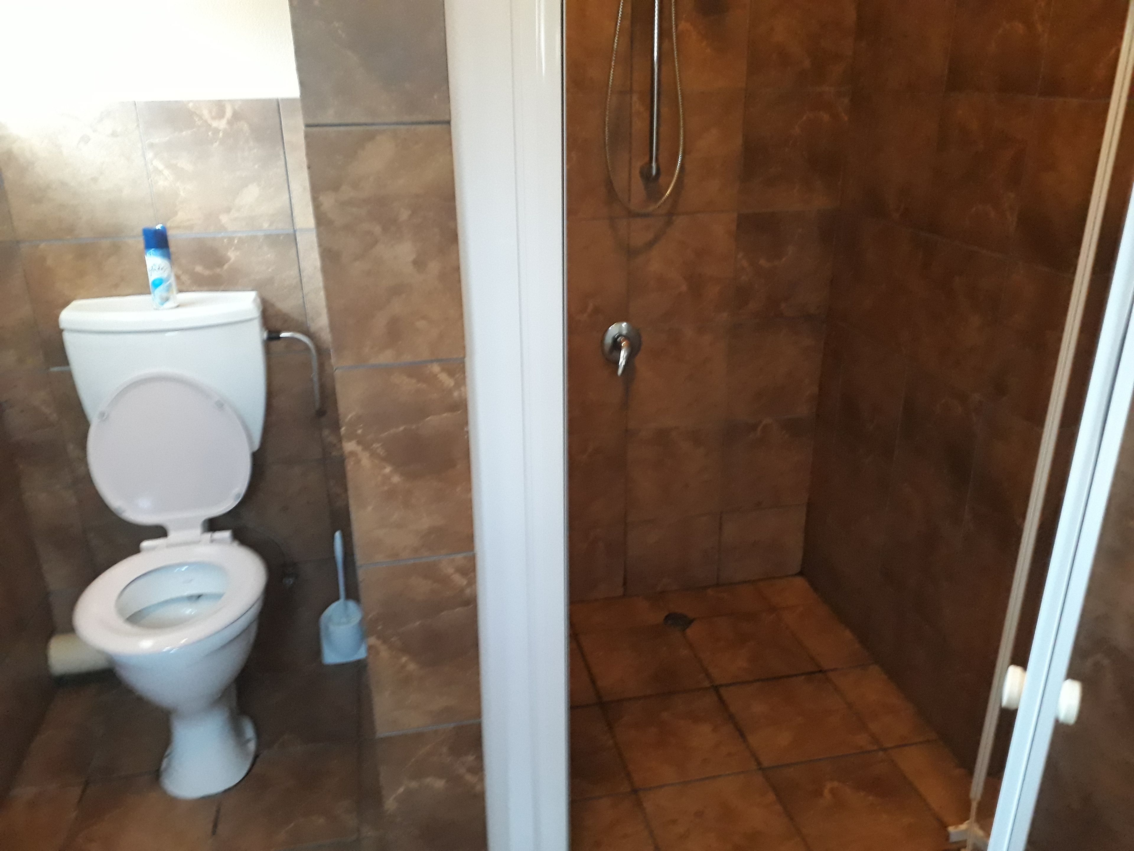 Une salle de bain avec des toilettes, une douche et un sol carrelé.