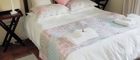 A neatly made bed with floral bedding, two bedside tables with lamps, a small rug, and a painting on the wall.