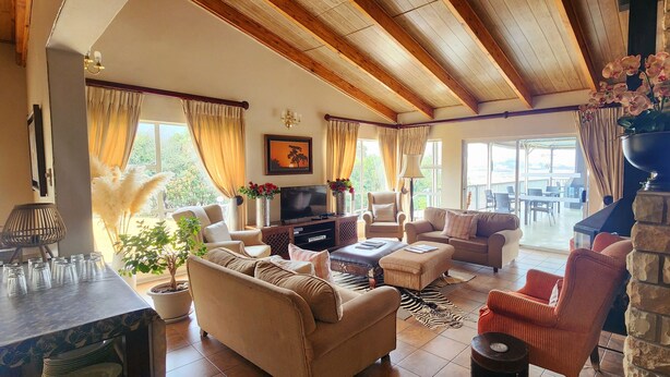 A spacious living room with a TV, sofas, chairs, and a stone pillar. - Ash River Lodge B&B (Clarens)
