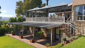 A two-story house with a covered patio, stone exterior, and a view of the landscape. - Ash River Lodge B&B (Clarens)