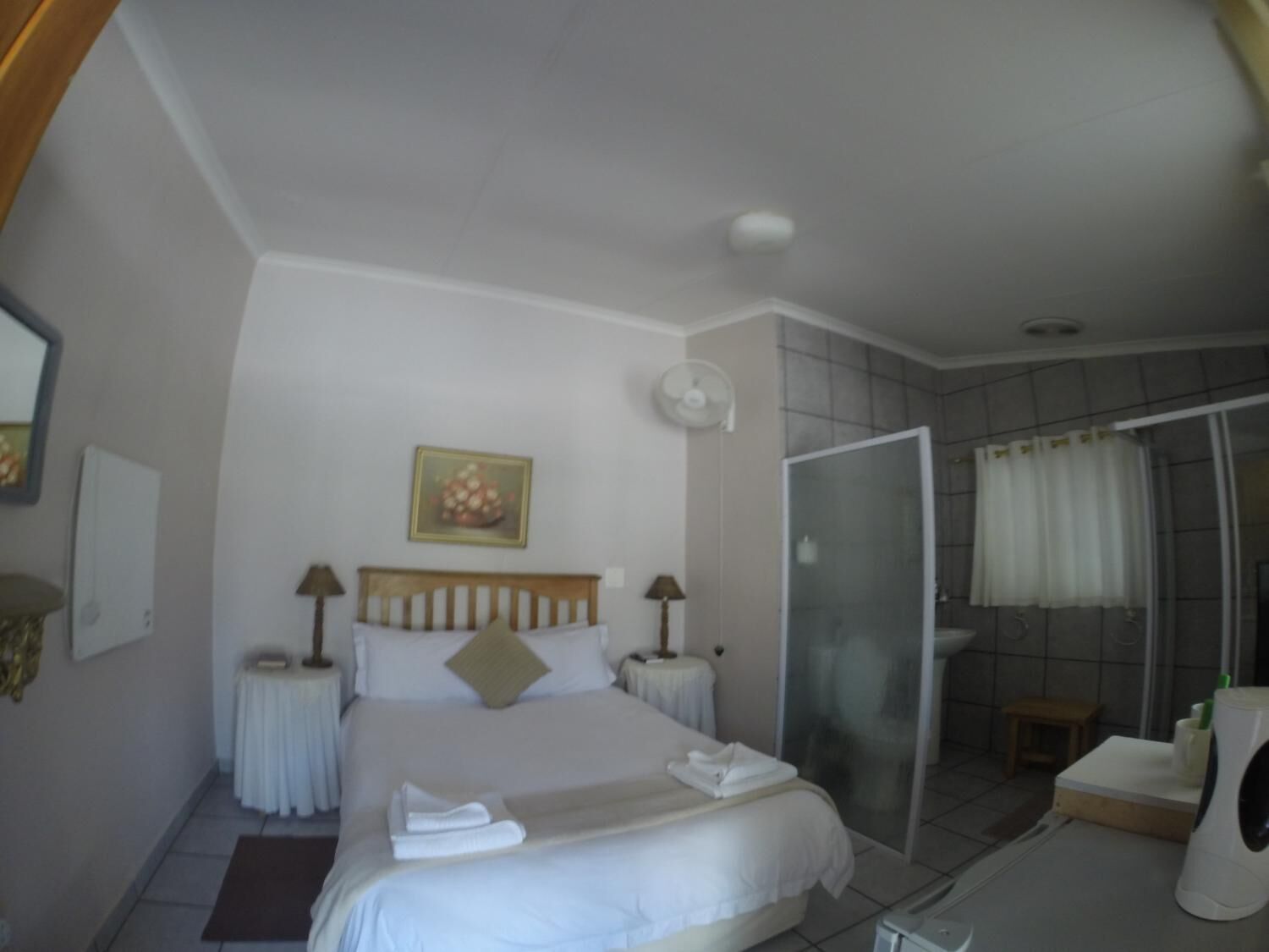 A hotel room with a bed, a bedside table, a lamp, a shower area, and a small stool.