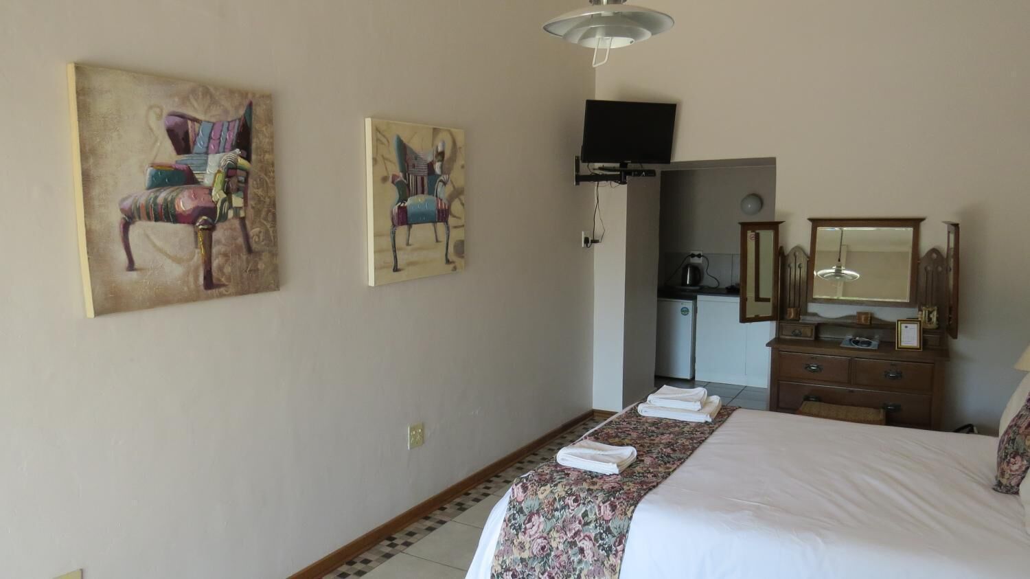 A hotel room with a bed, a TV, a dresser, and two paintings on the wall.