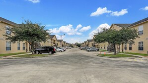 Une rue résidentielle bordée d’immeubles d’appartements, de voitures garées et d’arbres.