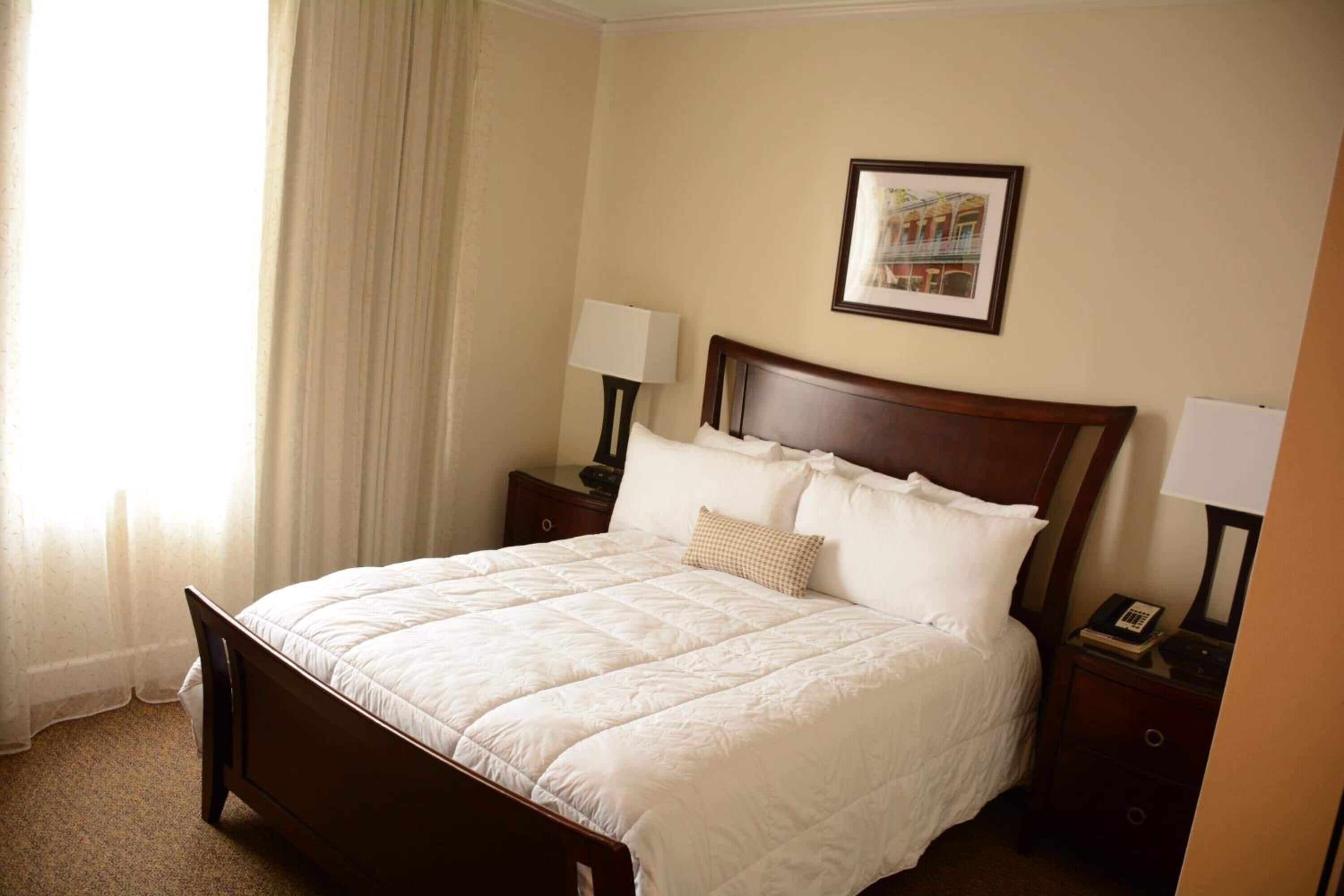 Une chambre d’hôtel avec un grand lit, deux tables de chevet avec des lampes, un tableau encadré au mur et une fenêtre avec des rideaux.