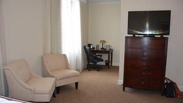 Quarto de hotel com cama, poltrona, escrivaninha com computador, cômoda e televisão.