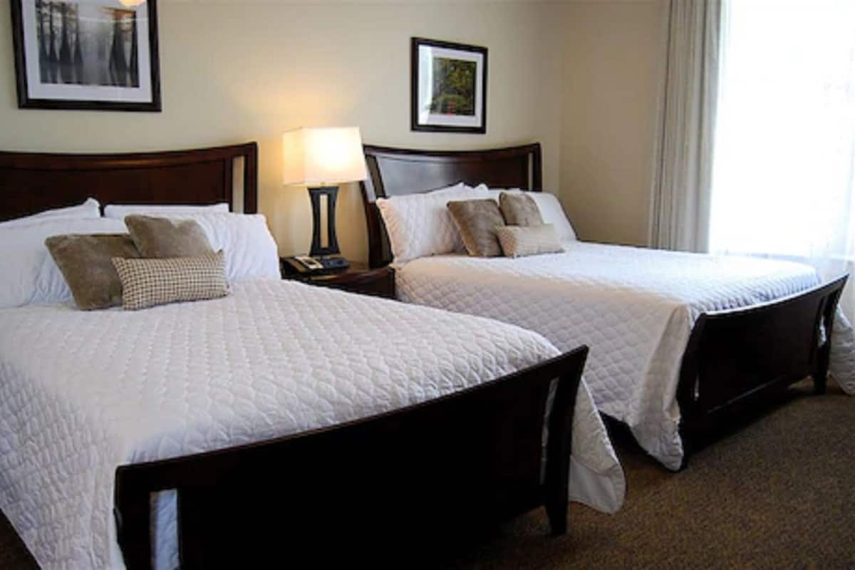 Une chambre d’hôtel avec deux lits « queen size », chacun doté d’une tête de lit en bois, de draps blancs et d’une table de chevet avec une lampe.