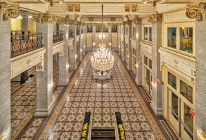 Un vaste hall d’hôtel, agrémenté d’un lustre central, de colonnes en marbre et de motifs décoratifs élaborés sur le sol.