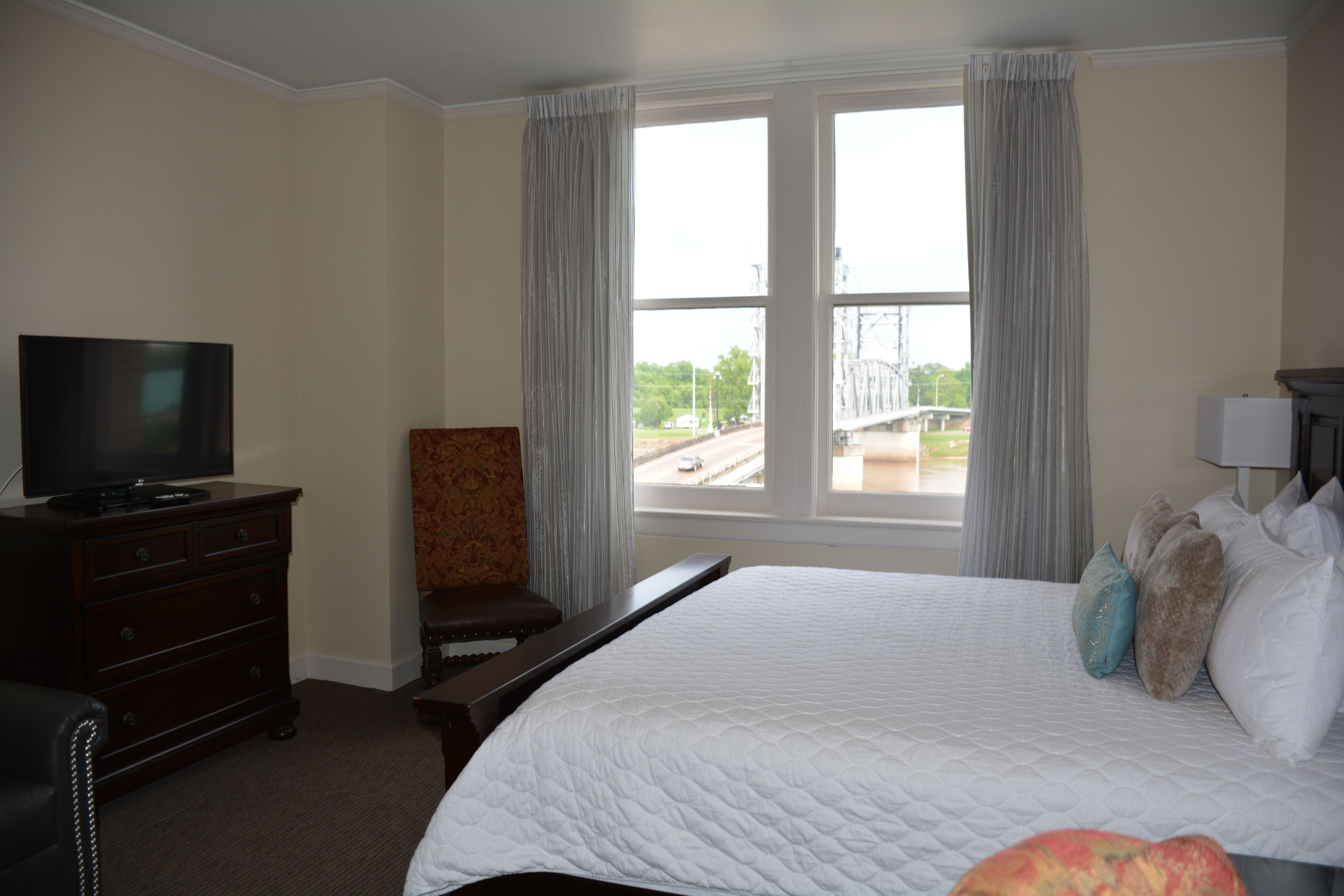 A hotel room with a large bed, a television on a dresser, a chair, and a window with a view of a bridge and road.