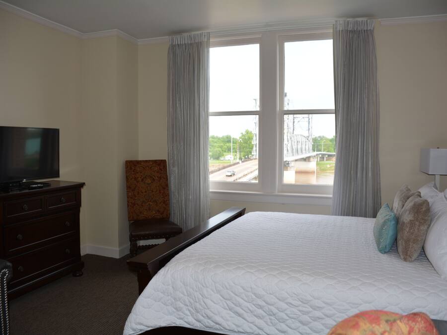 A hotel room with a large bed, a television on a dresser, a chair, and a window with a view of a bridge and road.