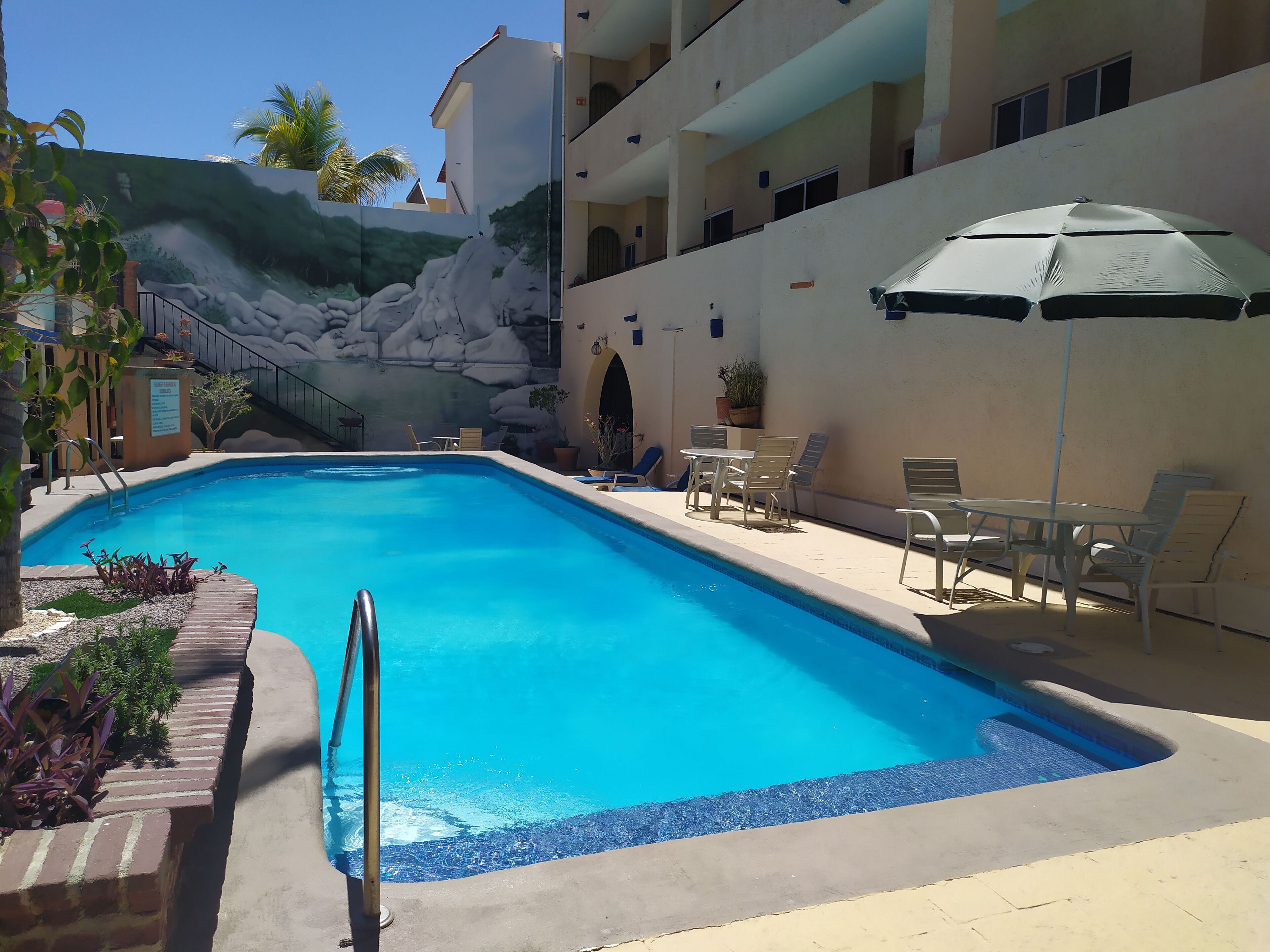 Ein Swimmingpool mit Wandmalerei, Liegestühlen und einem Tisch mit Sonnenschirm.