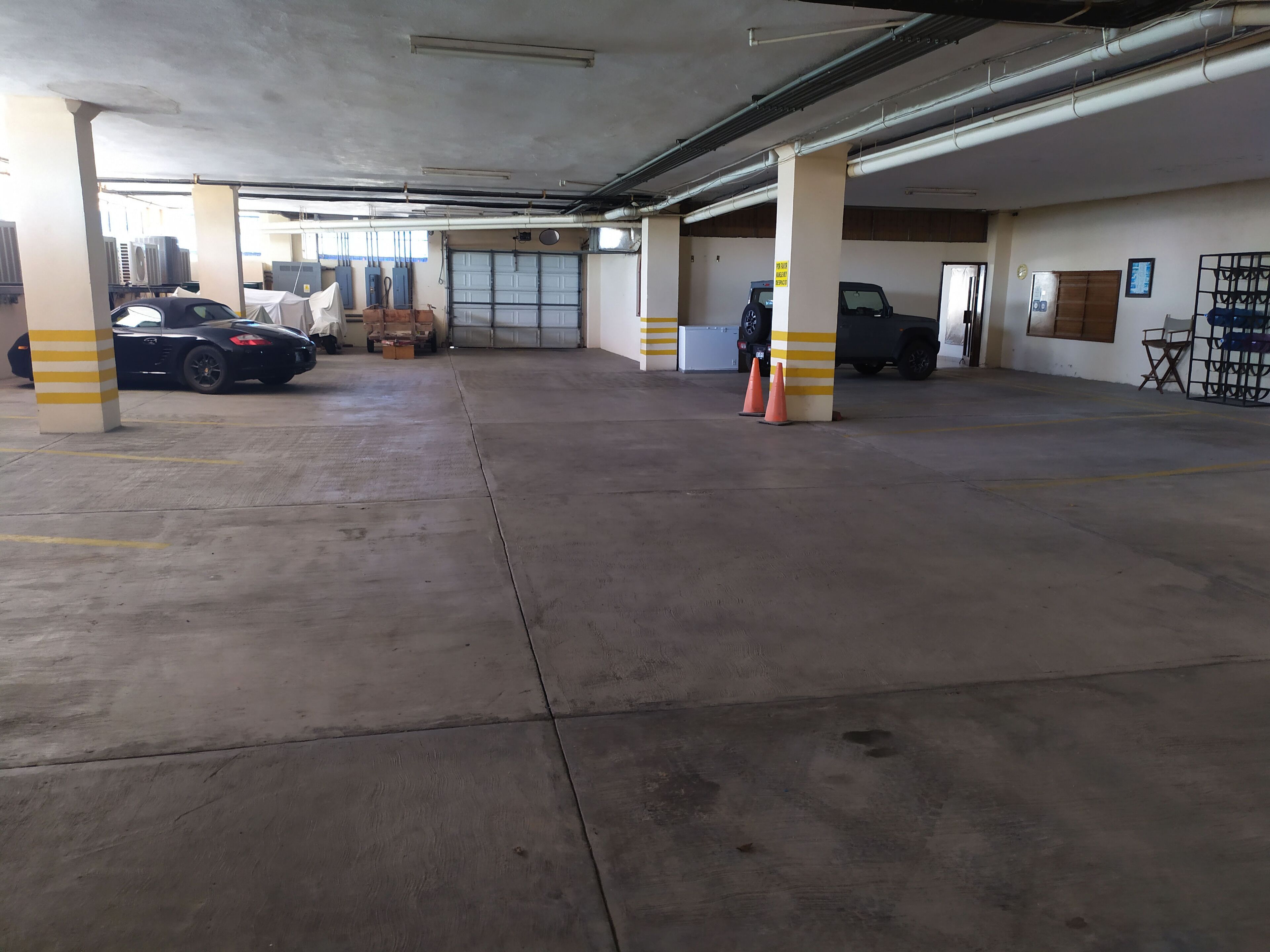 Eine Parkgarage mit Betonböden und -säulen, einigen Fahrzeugen und orangen Absperrtrichtern.