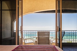 Un balcón con una cama, dos sillas y vista a la playa y el océano.